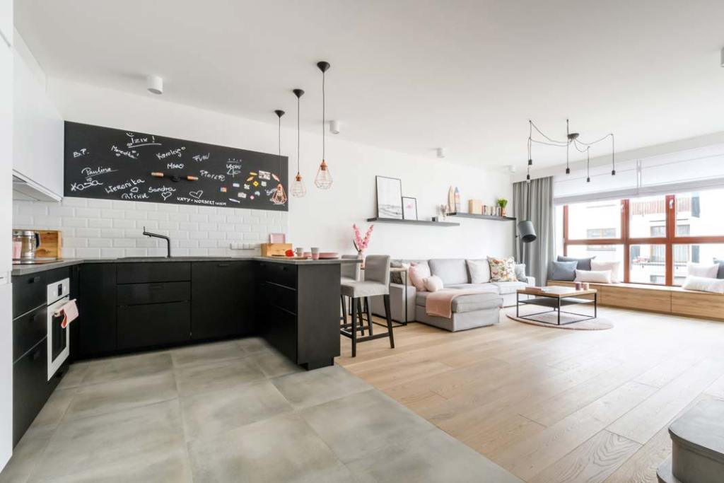 Jak dzielić przestrzeń_By wyznaczyć czytelną granicę między częścią kuchenną a salonową, Katarzyna Szostakowska z pracowni Kate&Co zestawiła materiały w kontrastowych kolorach: grafitowe płytki z parkietem w odcieniu bieli Dąb Biscuits Grande.