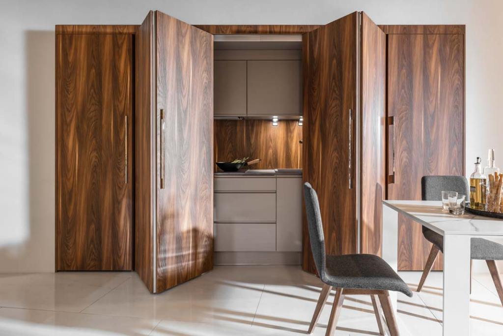 Kuchnia ukryta za otwieranymi harmonijkowo drzwiami to pomysł marki PEKA. Wysuwane z korpusu mebli drzwi, ukrywają część roboczą kuchni i ujednolicają wygląd połączonego z aneksem