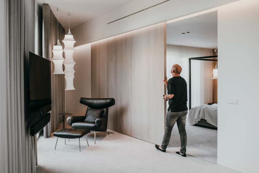 architekci z pracowni MMOA wyburzoną ścianę sypialni zastąpili drzwiami przesuwnymi z jasnego forniru dębowego. Zabieg sprawił, że sypialnia z garderobą i łazienką ma otwarty układ. Po rozsunięciu drzwi główną rolę w aranżacji odgrywa ogromne łóżko z baldachimem. Po ich zasunięciu część sypialniana jest niewidoczna.